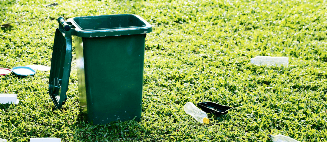 A green waste bin outdoors with discarded packaging on the grass